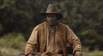 Movie still from “The Keeping Room” (2014), directed by Daniel Barber – A man with a beard and a hat sitting in a chair; Medium shot, Over the shoulder angle