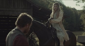 Movie still from “The Keeping Room” (2014), directed by Daniel Barber – A woman riding a horse next to a man in a barn; Medium shot, Over the shoulder angle
