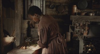Movie still from “The Keeping Room” (2014), directed by Daniel Barber – A woman standing in front of a table with food on top of it; Medium shot, Over the shoulder angle