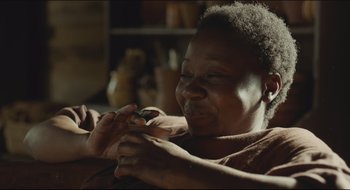 Movie still from “The Keeping Room” (2014), directed by Daniel Barber – An older woman sitting on a couch holding a remote; Close Up shot, Over the shoulder angle