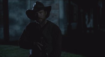 Movie still from “The Keeping Room” (2014), directed by Daniel Barber – A man wearing a cowboy hat and holding a gun; Medium shot, Over the shoulder angle