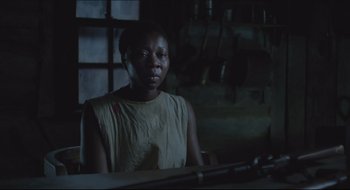 Movie still from “The Keeping Room” (2014), directed by Daniel Barber – A woman is sitting at a table in a dark room; Medium shot, Over the shoulder angle