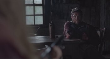 Movie still from “The Keeping Room” (2014), directed by Daniel Barber – A man sitting at a table with a knife in his hand; Medium shot, Over the shoulder angle
