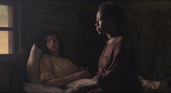 Movie still from “The Keeping Room” (2014), directed by Daniel Barber – A woman sitting next to another woman in a dark room; Medium shot, High angle
