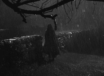 Movie still from “The Keys of the Kingdom” (1944), directed by John M. Stahl – A person standing in the rain near a tree; Wide shot, Low angle