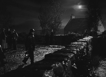 Movie still from “The Keys of the Kingdom” (1944), directed by John M. Stahl – A black and white photo of a group of people standing next to a stone wall at night; Extreme Wide shot, High angle