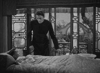 Movie still from “The Keys of the Kingdom” (1944), directed by John M. Stahl – A man standing next to a woman laying in a bed; Medium shot, High angle