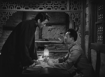 Movie still from “The Keys of the Kingdom” (1944), directed by John M. Stahl – Two men are sitting at a table and one of them is holding a bottle; Medium shot, Low angle