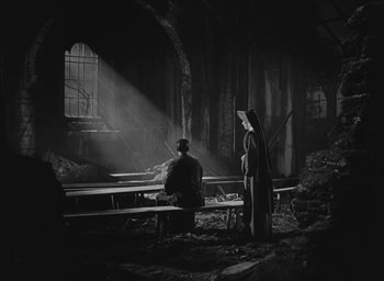 Movie still from “The Keys of the Kingdom” (1944), directed by John M. Stahl – Two people are sitting at a table in a dark room; Wide shot, Low angle