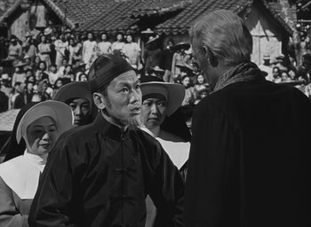 Movie still from “The Keys of the Kingdom” (1944), directed by John M. Stahl – An older man and a younger man are talking to each other in front of a crowd; Medium shot, Over the shoulder angle