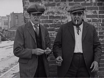 Movie still from “The Kid” (1921), directed by Charles Chaplin – A couple of men standing next to each other on a street; Medium shot, Low angle