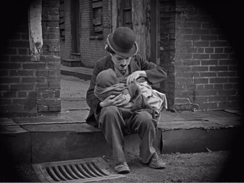 Movie still from “The Kid” (1921), directed by Charles Chaplin – An old photo of a man sitting on the steps holding a baby; Medium shot, High angle