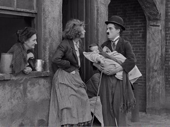 Movie still from “The Kid” (1921), directed by Charles Chaplin – An old photo of a man holding a baby and a woman; Medium shot, High angle