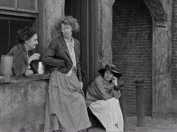 Movie still from “The Kid” (1921), directed by Charles Chaplin – A group of women sitting on the side of a brick building; Wide shot, Low angle