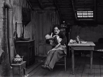 Movie still from “The Kid” (1921), directed by Charles Chaplin – An old man sitting in a chair holding a baby in his arms; Wide shot, High angle