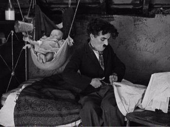 Movie still from “The Kid” (1921), directed by Charles Chaplin – An old black and white photo of a man and a baby; Medium shot, High angle