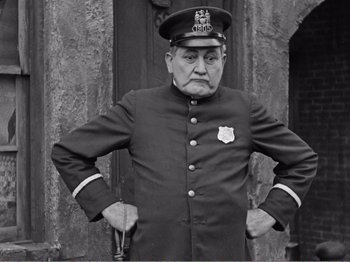 Movie still from “The Kid” (1921), directed by Charles Chaplin – An old man in a uniform is posing for a picture; Medium shot, Low angle