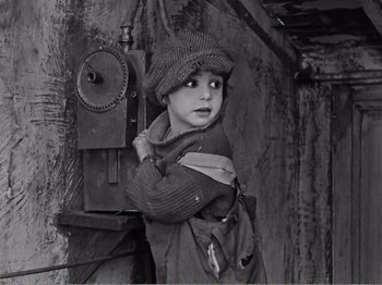 Movie still from “The Kid” (1921), directed by Charles Chaplin – A little boy standing in front of an electrical box; Medium shot, High angle