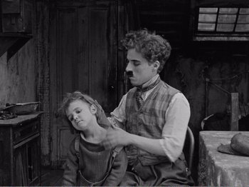Movie still from “The Kid” (1921), directed by Charles Chaplin – An old photo of a man cutting a young boy's hair; Medium shot, Over the shoulder angle