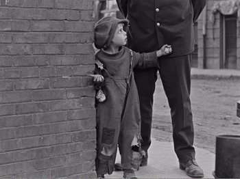 Movie still from “The Kid” (1921), directed by Charles Chaplin – A little boy standing next to an older man; Medium shot, Low angle