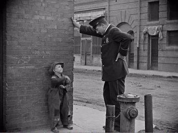 Movie still from “The Kid” (1921), directed by Charles Chaplin – An old photo of a man and a little boy; Wide shot, Over the shoulder angle