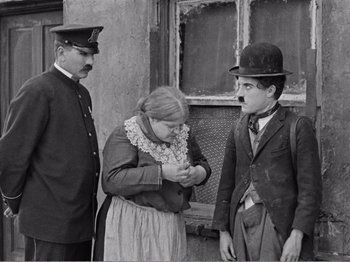 Movie still from “The Kid” (1921), directed by Charles Chaplin – A man and a woman standing next to a man in a hat; Medium shot, Over the shoulder angle