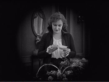 Movie still from “The Kid” (1921), directed by Charles Chaplin – A woman is looking down at a piece of paper in her hands; Medium shot, High angle