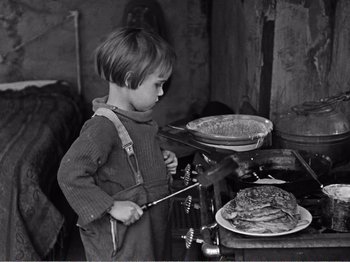 Movie still from “The Kid” (1921), directed by Charles Chaplin – A little boy standing in front of a pan of food on a stove; Medium shot, High angle