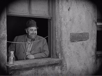 Movie still from “The Kid” (1921), directed by Charles Chaplin – An older man sitting in a window sill; Medium shot, Low angle