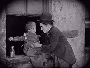 Movie still from “The Kid” (1921), directed by Charles Chaplin – An old black and white photo of a man and a child; Medium shot, Low angle