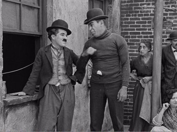 Movie still from “The Kid” (1921), directed by Charles Chaplin – Two men and a woman wearing hats and holding hands; Medium shot, Low angle