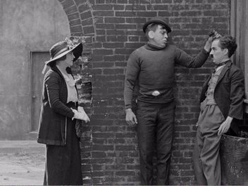 Movie still from “The Kid” (1921), directed by Charles Chaplin – An old photo of a group of people standing next to a brick wall; Medium shot, Over the shoulder angle