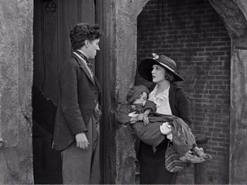 Movie still from “The Kid” (1921), directed by Charles Chaplin – An old photo of a man and a woman holding a baby; Medium shot, Over the shoulder angle