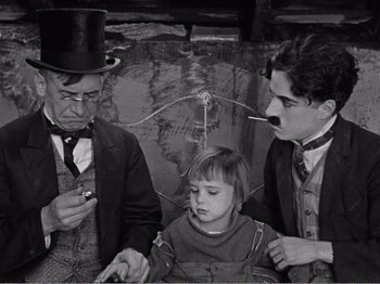 Movie still from “The Kid” (1921), directed by Charles Chaplin – A group of people that are standing up; Medium shot, High angle