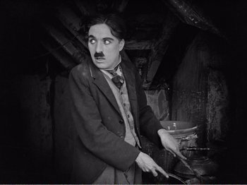 Movie still from “The Kid” (1921), directed by Charles Chaplin – An old photo of a man holding a knife; Medium shot, High angle