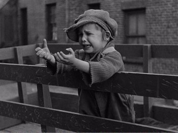 Movie still from “The Kid” (1921), directed by Charles Chaplin – A little boy that is sitting on top of a bench; Medium shot, High angle