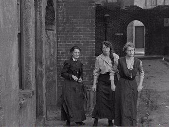 Movie still from “The Kid” (1921), directed by Charles Chaplin – A group of women standing next to each other on a street; Wide shot, Low angle