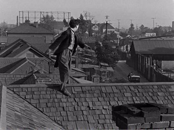 Movie still from “The Kid” (1921), directed by Charles Chaplin – A man standing on top of a brick roof; Wide shot, High angle