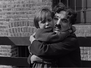 Movie still from “The Kid” (1921), directed by Charles Chaplin – A man and a boy hugging each other in front of a brick building; Close Up shot, High angle
