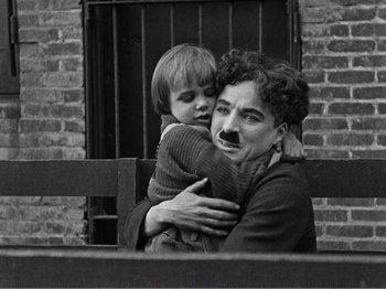 Movie still from “The Kid” (1921), directed by Charles Chaplin – An older woman holding a young boy in her arms; Medium shot, High angle