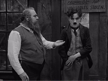 Movie still from “The Kid” (1921), directed by Charles Chaplin – A man with a long beard and a man with a mustache; Medium shot, Over the shoulder angle