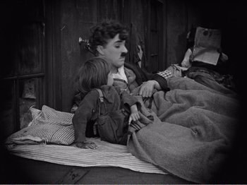 Movie still from “The Kid” (1921), directed by Charles Chaplin – An old photo of a woman and a child laying on the ground; Medium shot, High angle