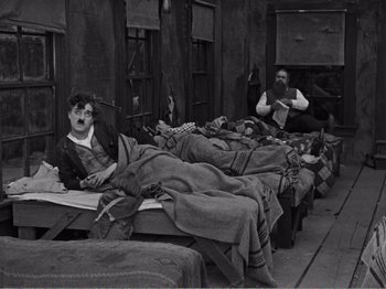 Movie still from “The Kid” (1921), directed by Charles Chaplin – A man and a woman are sleeping on a bed; Wide shot, High angle