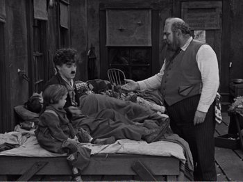 Movie still from “The Kid” (1921), directed by Charles Chaplin – An old black and white photo of two men and two children; Wide shot, High angle