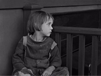 Movie still from “The Kid” (1921), directed by Charles Chaplin – A young boy sitting on a wooden railing; Medium shot, High angle