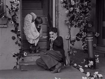 Movie still from “The Kid” (1921), directed by Charles Chaplin – An old photo of a woman sitting on the steps with a child; Wide shot, High angle