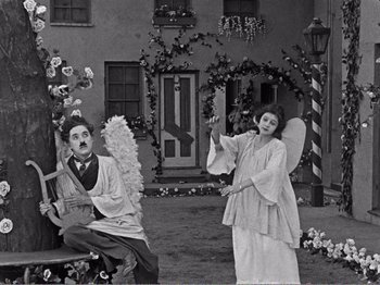 Movie still from “The Kid” (1921), directed by Charles Chaplin – A man and a woman dressed as angel and cherub; Wide shot, High angle