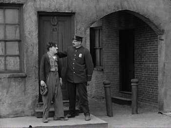 Movie still from “The Kid” (1921), directed by Charles Chaplin – Two men standing in front of a building; Wide shot, Over the shoulder angle