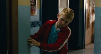 Movie still from “The Kid with a Bike” (2011), directed by Jean-Pierre Dardenne – A boy in a red jacket is opening a door; Medium shot, Over the shoulder angle