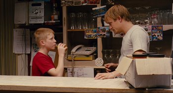 Movie still from “The Kid with a Bike” (2011), directed by Jean-Pierre Dardenne – A man and a boy at a counter eating a donut; Medium shot, Over the shoulder angle